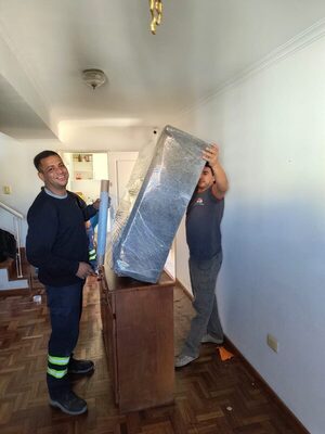 Dos operarios de Córdoba Fletes moviendo un mueble embalado en un living